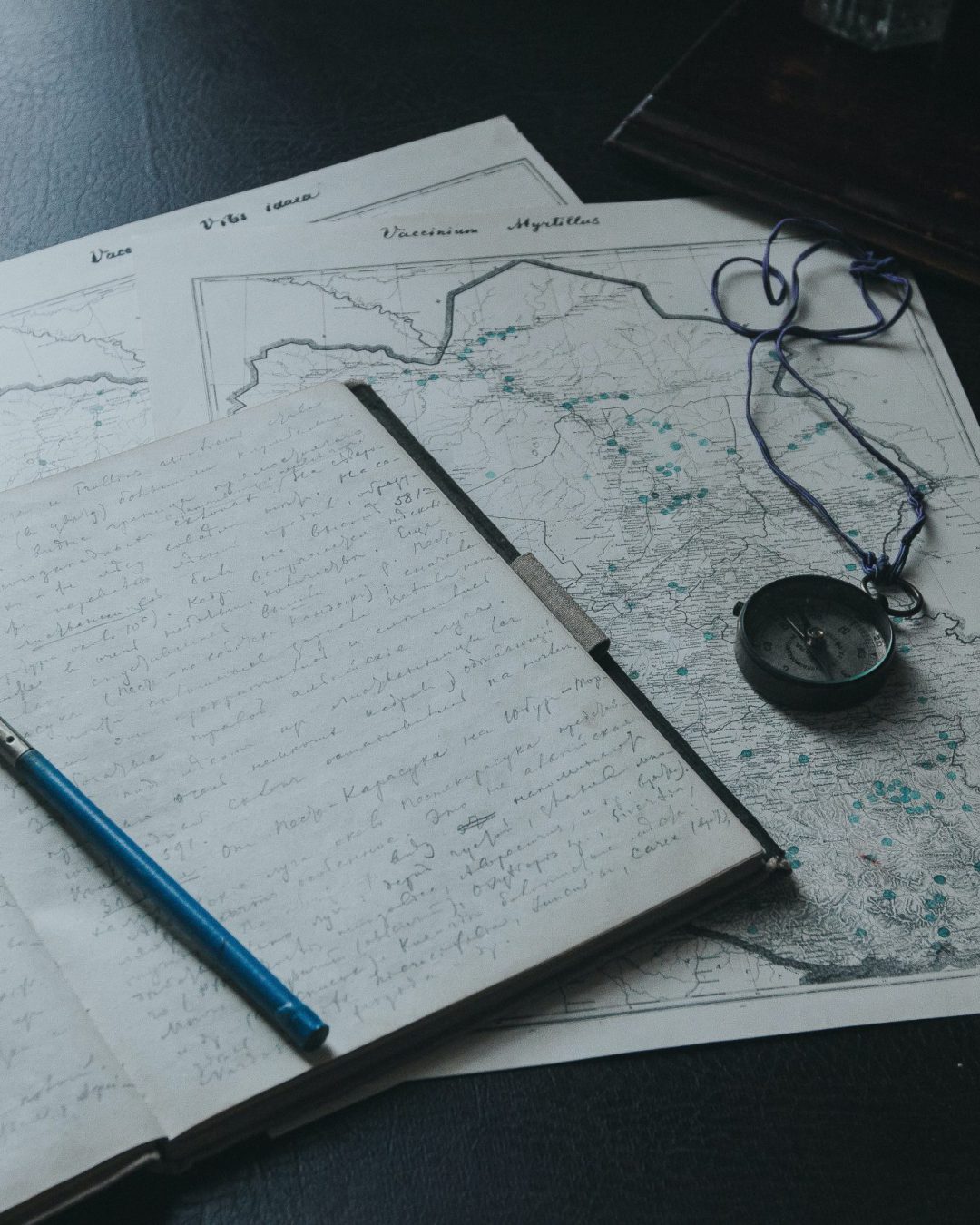 Caneta-tinteiro, caderno manuscrito e bússola sobre um mapa